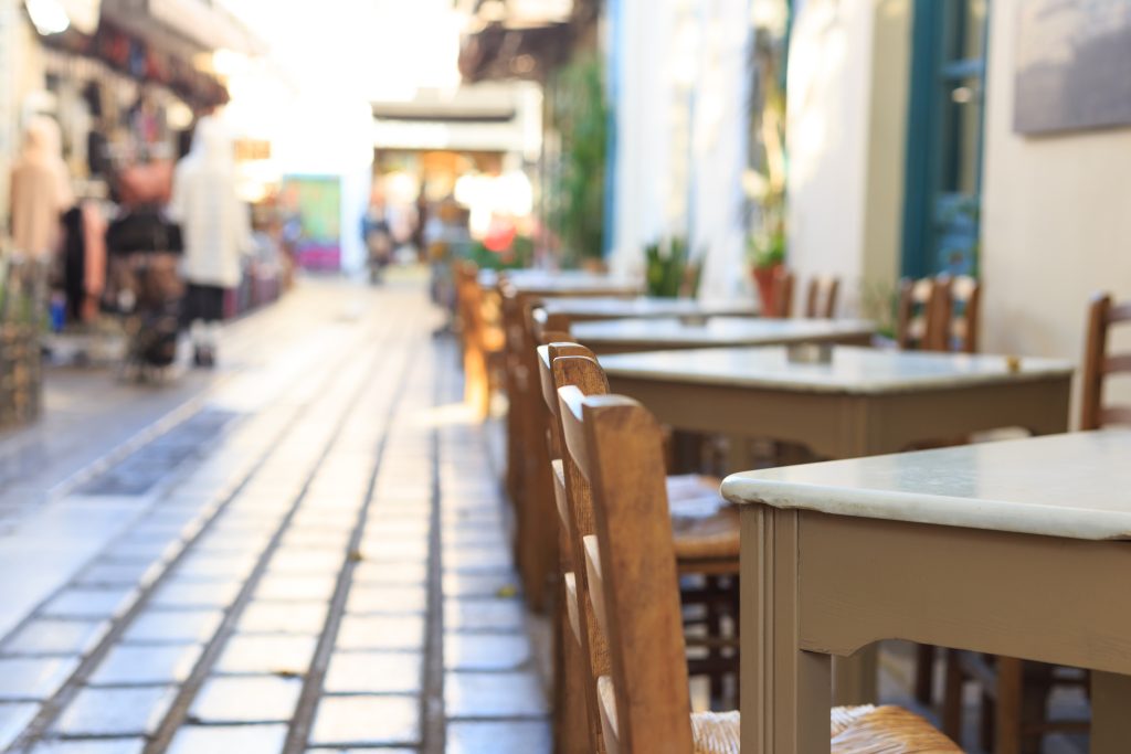 Athens, Greece. Greek tavern empty tables and chairs in a row, blur pedestrian and market background